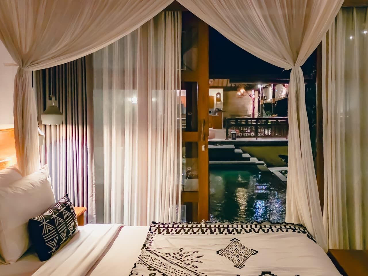 Ein Schlafzimmer mit Bett, Vorhängen und Blick auf einen Pool.