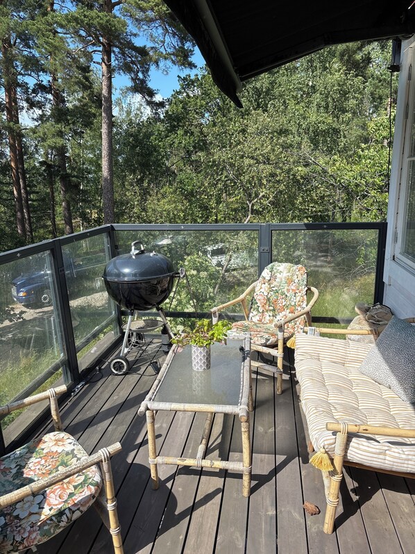 Una terraza techada con mobiliario de mimbre, una parrilla y una mesa de vidrio.