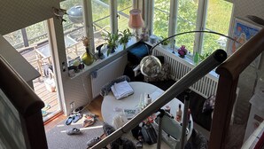 Korkeakattoinen huone, jossa on suuret ikkunat, pyöreä pöytä ja portaikko.