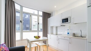 Una cocina moderna con armarios blancos, un microondas y un lavabo. Hay una mesa de comedor con sillas y un cuenco de fruta.
