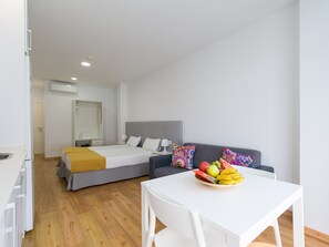 A modern hotel room with a bed, a sofa, a dining table with fruit, and a kitchenette. - Apartment in Las Palmas Near Las Canteras Beach (Las Palmas de Gran Canaria)