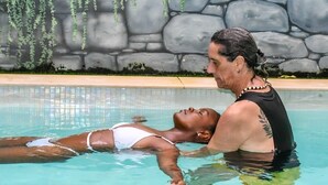 Una piscina con una pared de piedra y plantas colgantes al fondo.