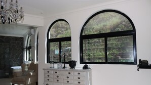 Un salón amplio con un gran ventanal de arco, un aparador blanco, un sillón color beige y una araña.