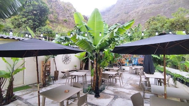 Un patio al aire libre con mesas y sillas, rodeado de abundante vegetación y montañas al fondo.