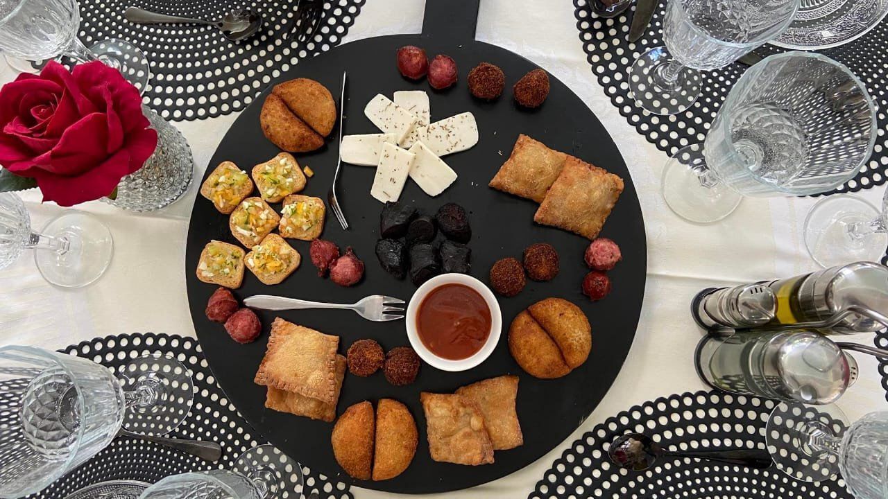 A dining table set with a black plate of assorted appetizers, a red rose, and clear glassware.