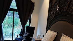 Un dormitorio con una cama grande, una silla, una mesita de noche y una ventana con cortinas.