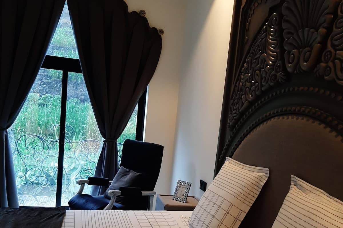 A bedroom with a large bed, a chair, a nightstand, and a window with curtains.