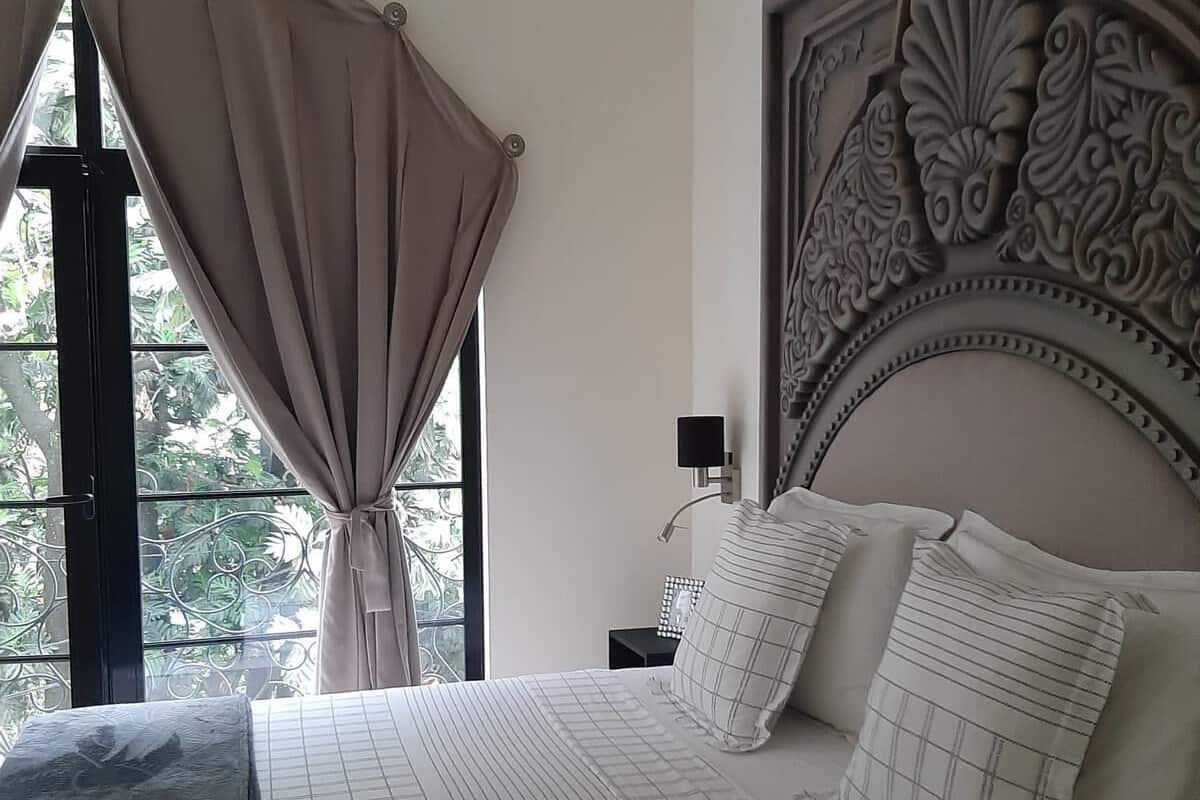 A bedroom with a large bed, a decorative headboard, and a window with curtains.