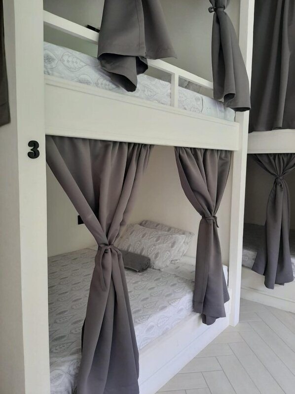 Un lit superposé avec des rideaux gris attachés aux coins, une tête de lit blanche et le chiffre « 3 » peint sur le mur.