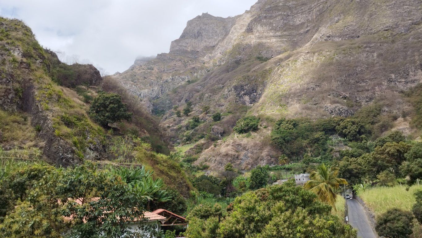 Un paysage montagneux avec une route, de la végétation et un bâtiment doté d’un toit rouge.