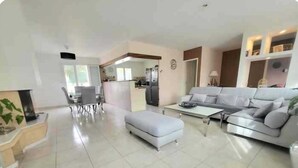 A spacious living room with a grey sofa, a white ottoman, and a dining area with a table and chairs.