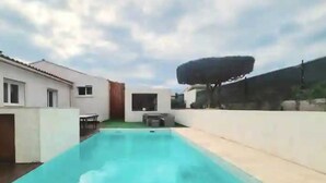 A swimming pool with a view of a modern house and a large umbrella.