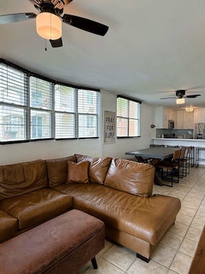 A modern living room with a leather sectional sofa, a dining area with a table and chairs, and a kitchen in the background.
