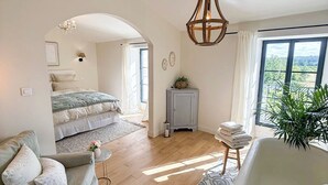 A spacious bedroom with a large bed, a sitting area with a sofa and a small table, and a bathroom with a bathtub and a large window.