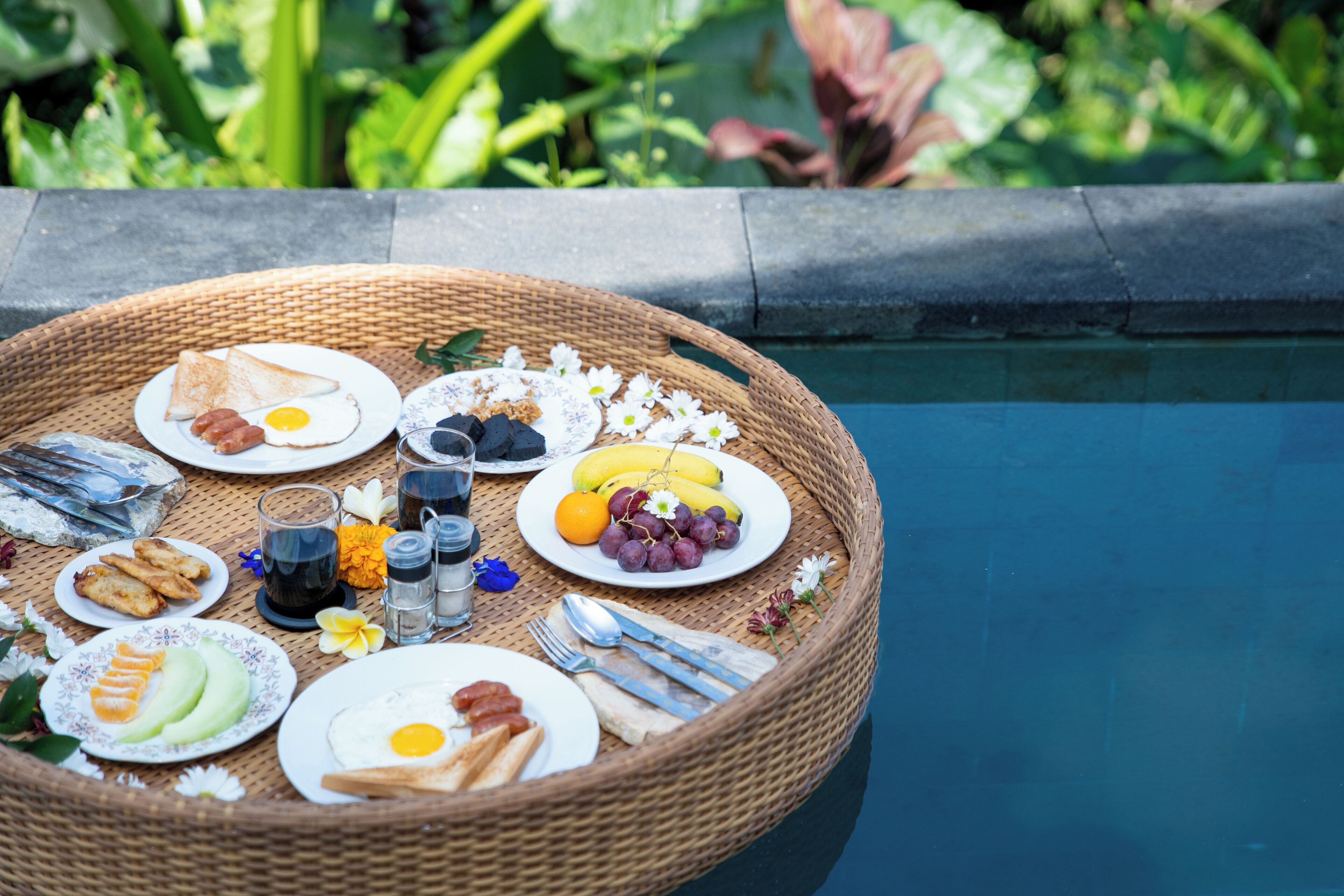 A breakfast setup on a poolside table with various food items and utensils.