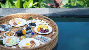 A breakfast setup on a poolside table with various food items and utensils.