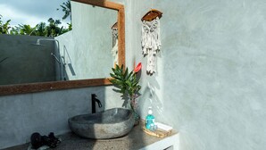 A bathroom with a large mirror, a stone sink, a wooden shelf with a soap dispenser, and a macramé wall hanging. - Sayuban Villa (Bangli)