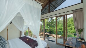 A bedroom with a canopy bed, a dining table, and a view of lush greenery outside. - Sayuban Villa (Bangli)