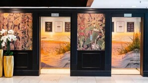 A reception area with three framed floral artworks on the wall, a potted plant, and a tiled floor. - Suite auf Wolke 7 von OstseeAhoi (Timmendorfer Strand)