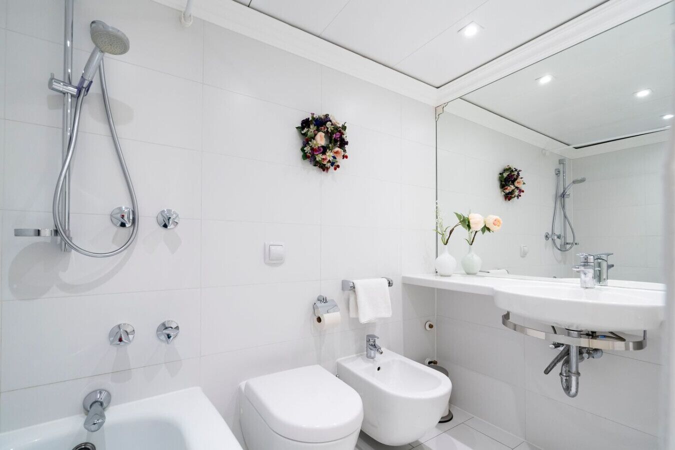 A modern bathroom with a bathtub, toilet, bidet, and a large mirror.