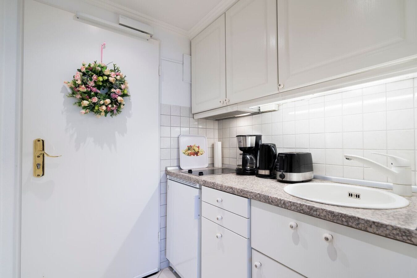 A kitchen with white cabinets, a granite countertop, a coffee maker, and a sink.