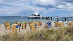 A beach with beach huts, a pier, and a building in the background. - Suite auf Wolke 7 von OstseeAhoi (Timmendorfer Strand)