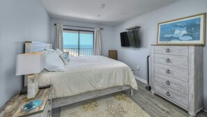 A bedroom with a bed, a dresser, a TV, and a view of the ocean.