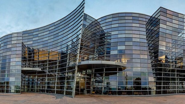 A modern glass building with a curved facade and a covered entrance area.