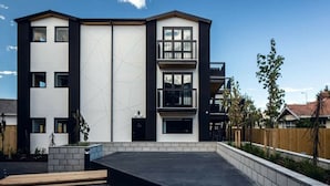 A modern multi-story residential building with a flat roof, large windows, and a balcony on the upper floor.