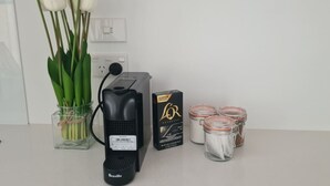 Una cafetera Breville, una caja de cápsulas L'Oréal, un jarrón con tulipanes blancos y tres frascos de vidrio con tapas.