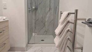 Un baño moderno con cabina de ducha de vidrio, suelo de mármol y un perchero.