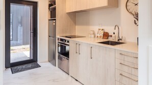 A modern kitchen with light wood cabinets, a stainless steel refrigerator, and a built-in oven.