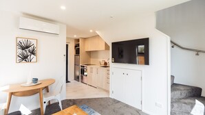 A modern apartment with a kitchen, dining area, and living space. It includes a flat-screen TV, a dining table with chairs, and a staircase.