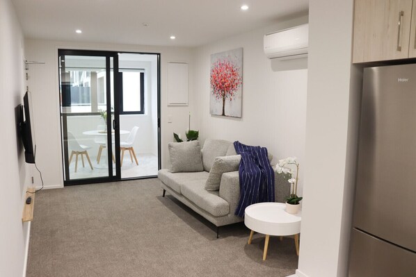 A modern living room with a grey sofa, a round white table, and a flat-screen TV mounted on the wall.