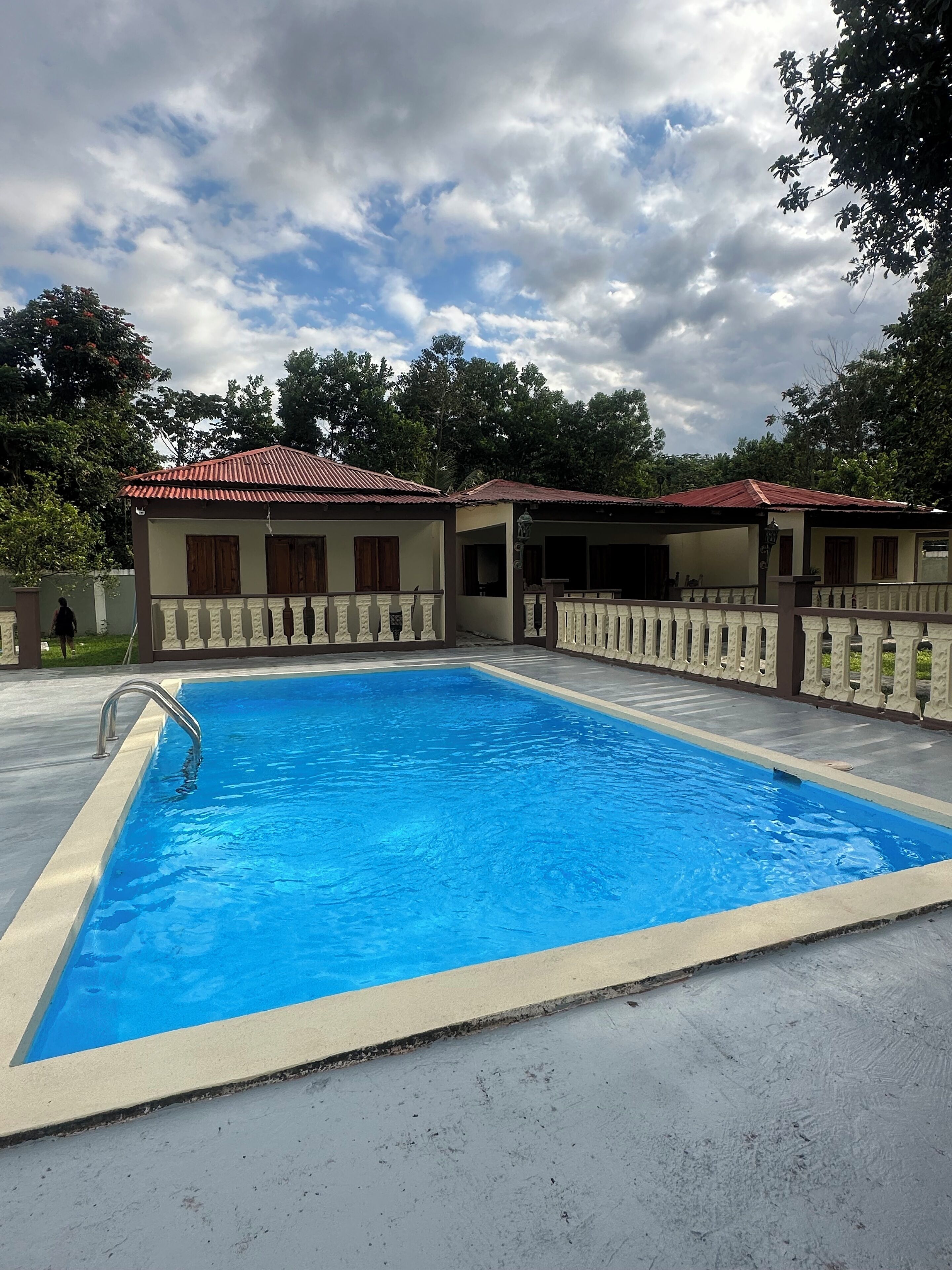 Une piscine dotée d’une terrasse carrelée, entourée d’une petite clôture et bordée d’un bâtiment au toit rouge.