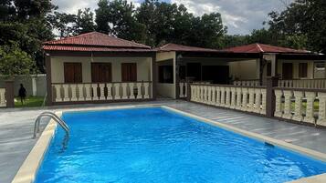 Une piscine dotée d’une terrasse carrelée, entourée d’une petite clôture et bordée d’un bâtiment au toit rouge.