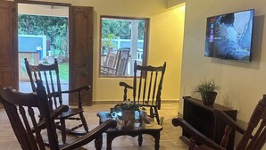 A living room with four wooden rocking chairs, a coffee table, a television on the wall, and a potted plant. - Soothing 4-bedroom country house in Piedra Blanca (Piedra Blanca)