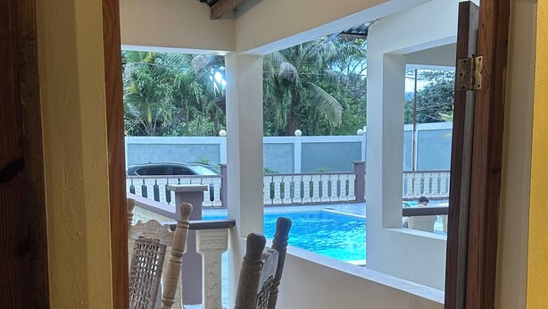 A view through a window of a room with a pool, wooden furniture, and a balcony with a railing. - Soothing 4-bedroom country house in Piedra Blanca (Piedra Blanca)