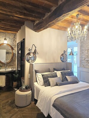 A bedroom with a large bed, a nightstand, a dresser, a mirror, and a chandelier. - The little guest house (Lucca)