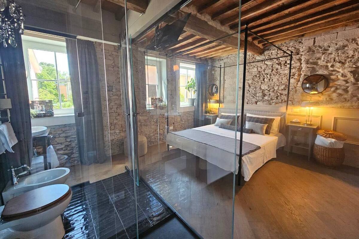 Un dormitorio moderno con cabina de ducha de vidrio, una cama grande y una pared de piedra.