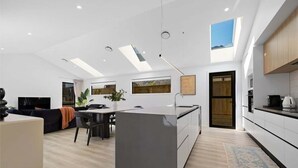 A modern kitchen with a central island, skylights, and a dining area with a sofa and table.