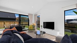 A modern living room with a large TV, comfortable seating, and a view of the outdoors.