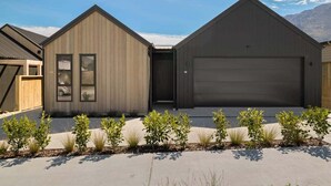 A modern two-story house with a garage, a small porch, and a landscaped front yard with shrubs.