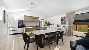 A modern kitchen with a dining area, featuring a marble table, black chairs, and a potted plant.