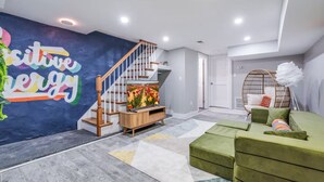 Una sala de estar moderna con una escalera, un televisor de pantalla plana, un sofá verde y una pared decorativa con una frase motivacional.