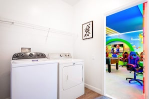 A laundry area with a front-loading washer and dryer, a wall-mounted shelf, and a framed picture.