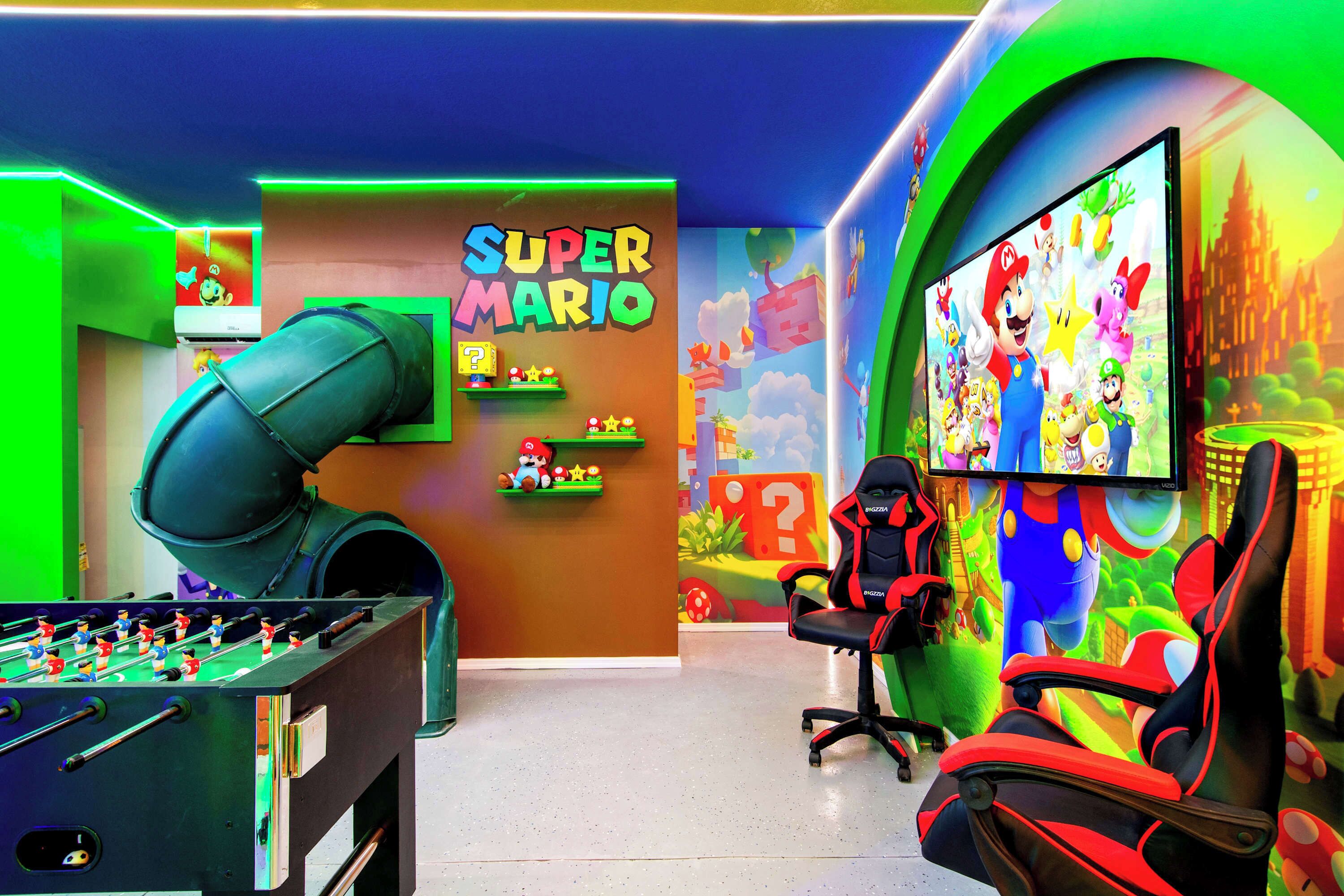 A gaming room with a foosball table, a large screen, and a Super Mario themed wall.