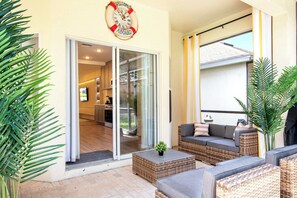 A modern outdoor seating area with wicker furniture and a glass door leading to a kitchen. - Mario, Mickey & Jedi Arcade Villa w/ Themed Rooms (Kissimmee)