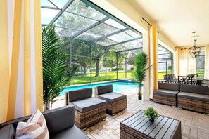 A covered outdoor area with wicker furniture, a pool, and a view of the surrounding greenery. - Mario, Mickey & Jedi Arcade Villa w/ Themed Rooms (Kissimmee)
