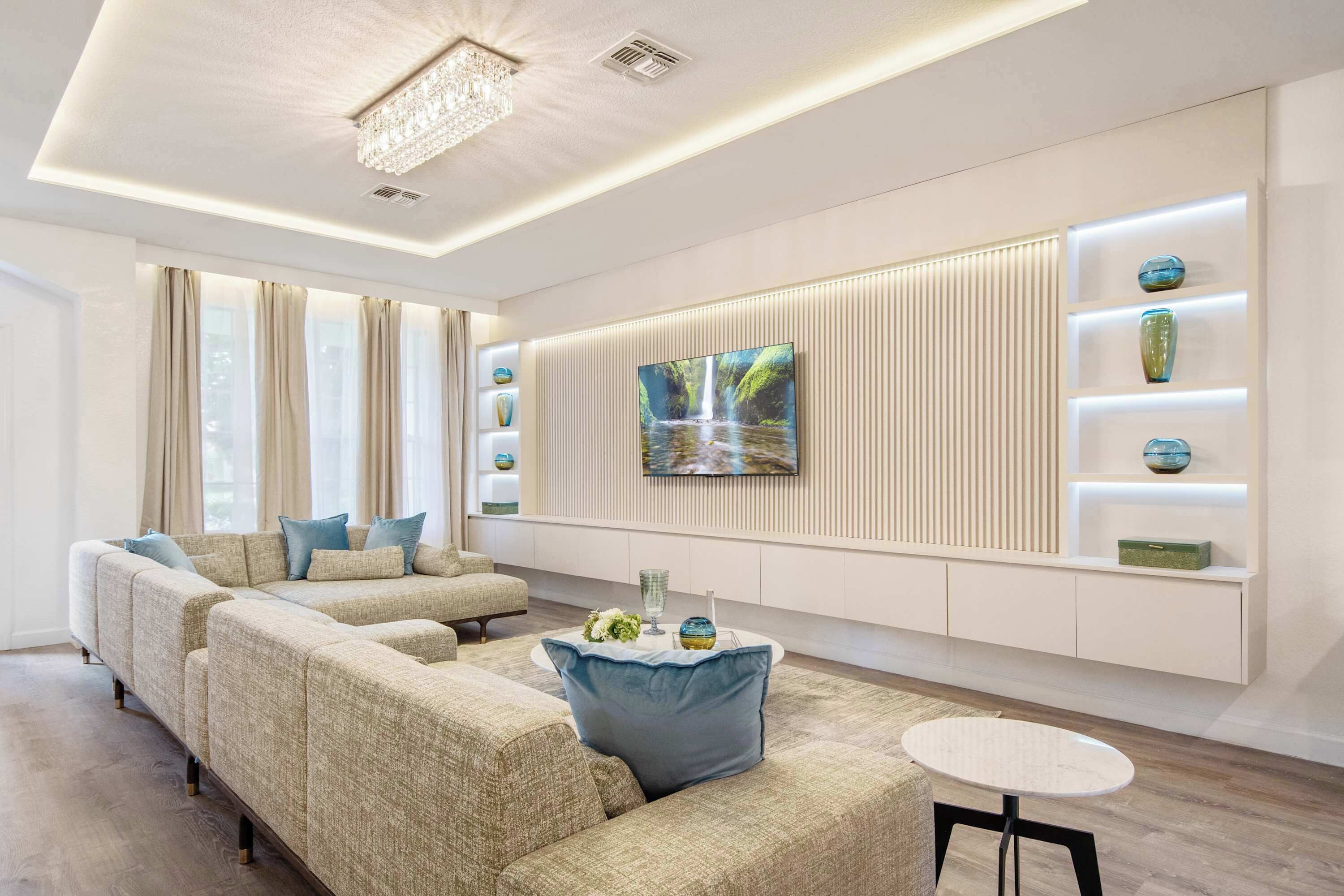 A modern living room with a sectional sofa, a round coffee table, and a flat-screen TV mounted on a wall with built-in shelving.
